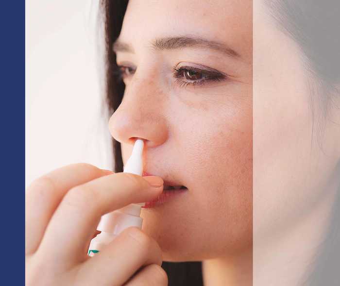 Frau sprüht sich Nasenspray in ein Nasenloch