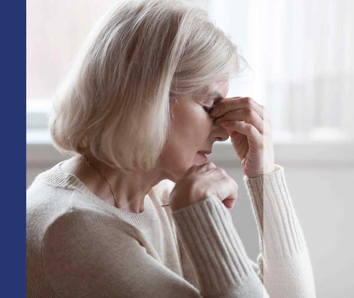 Frau mit Schmerzen hält sich mit geschlossenen Augen den Nasenrücken