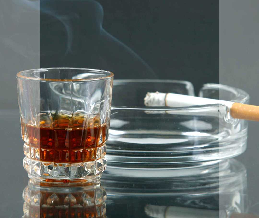 Aschenbecher mit qualmender Zigarette und ein Glas mit Alkohol.