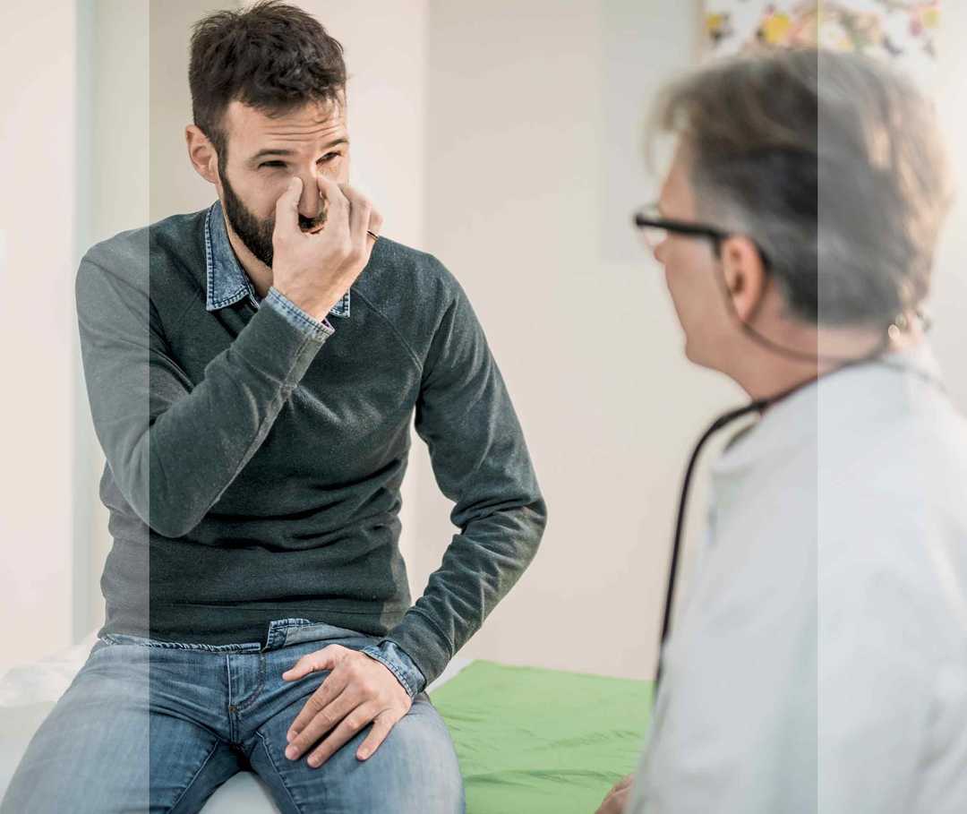 Mann beim Arzt reibt sich die verstopfte Nase