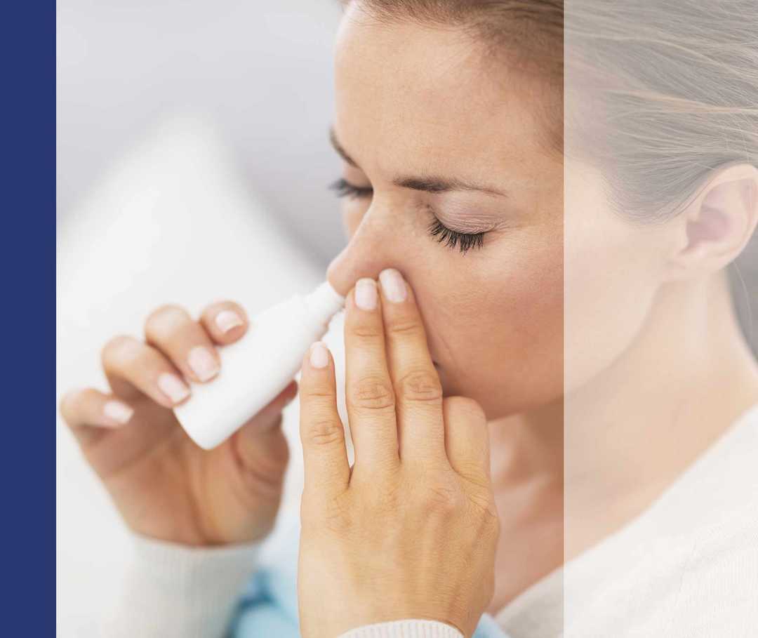 Frau sprüht Nasenspray in ein Nasenloch