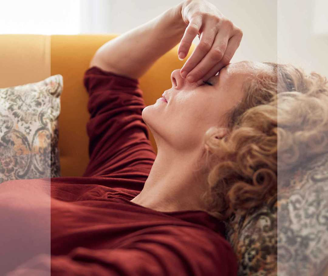 Frau liegt auf einem Sofa und reibt sich den Nasenrücken