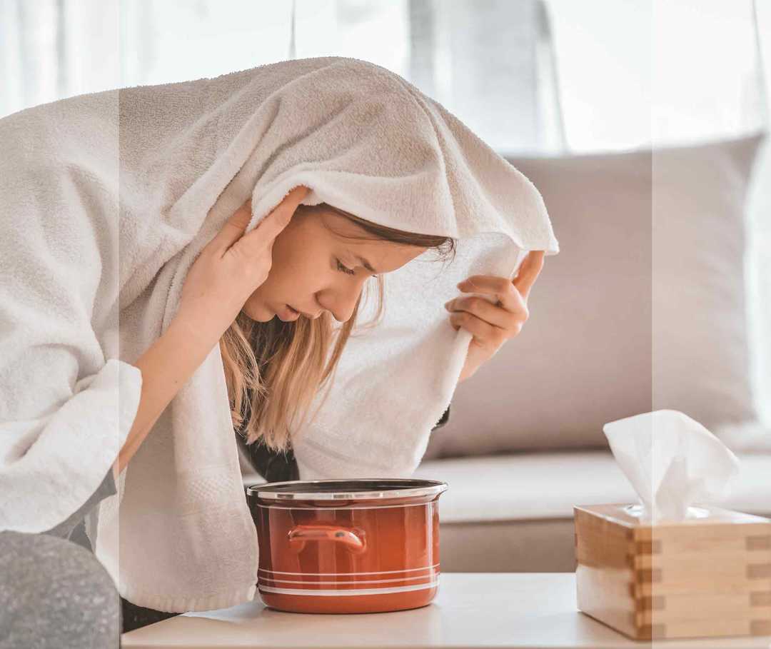 Eine Frau inhaliert mit einem Handtuch über dem Kopf.