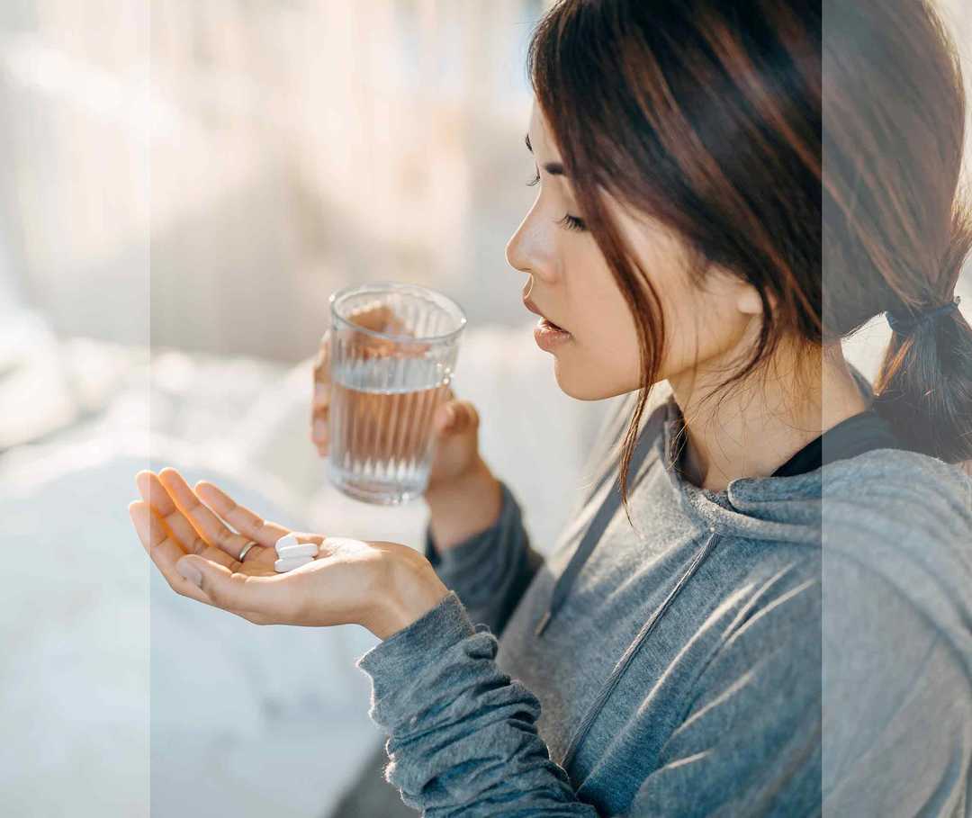 Junge Frau mit Wasserglas in der Hand nimmt ein Medikament.